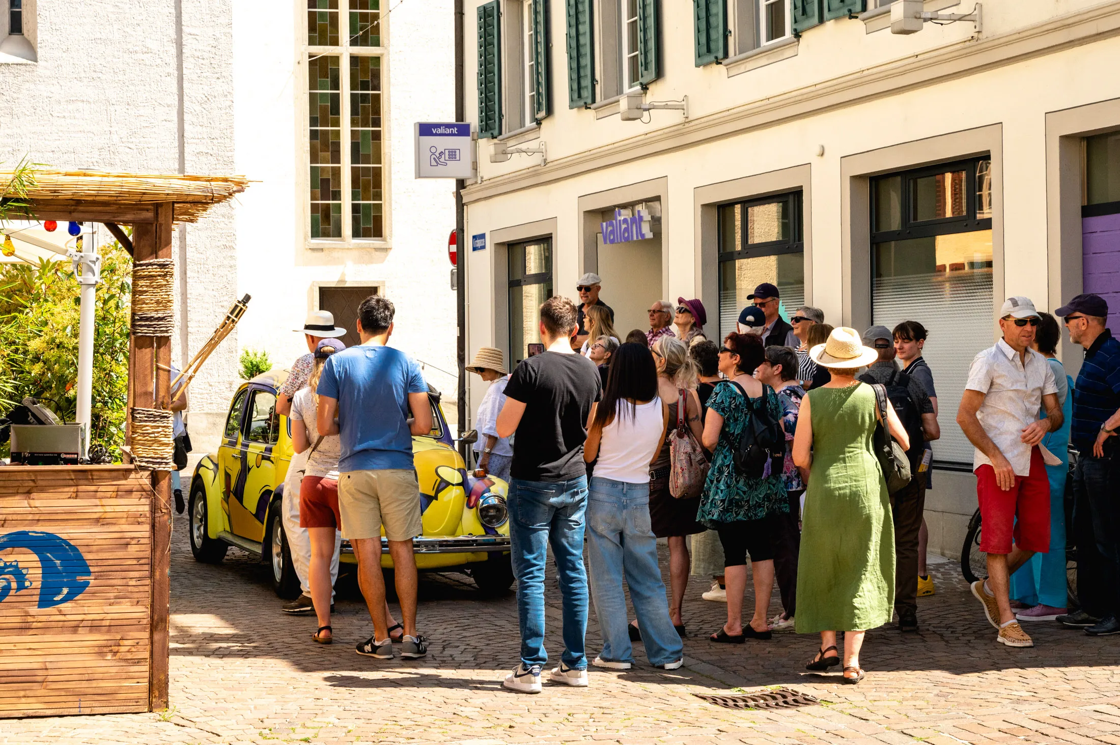 A guided tour group in an old town lane, a yellow painted Beetle in front