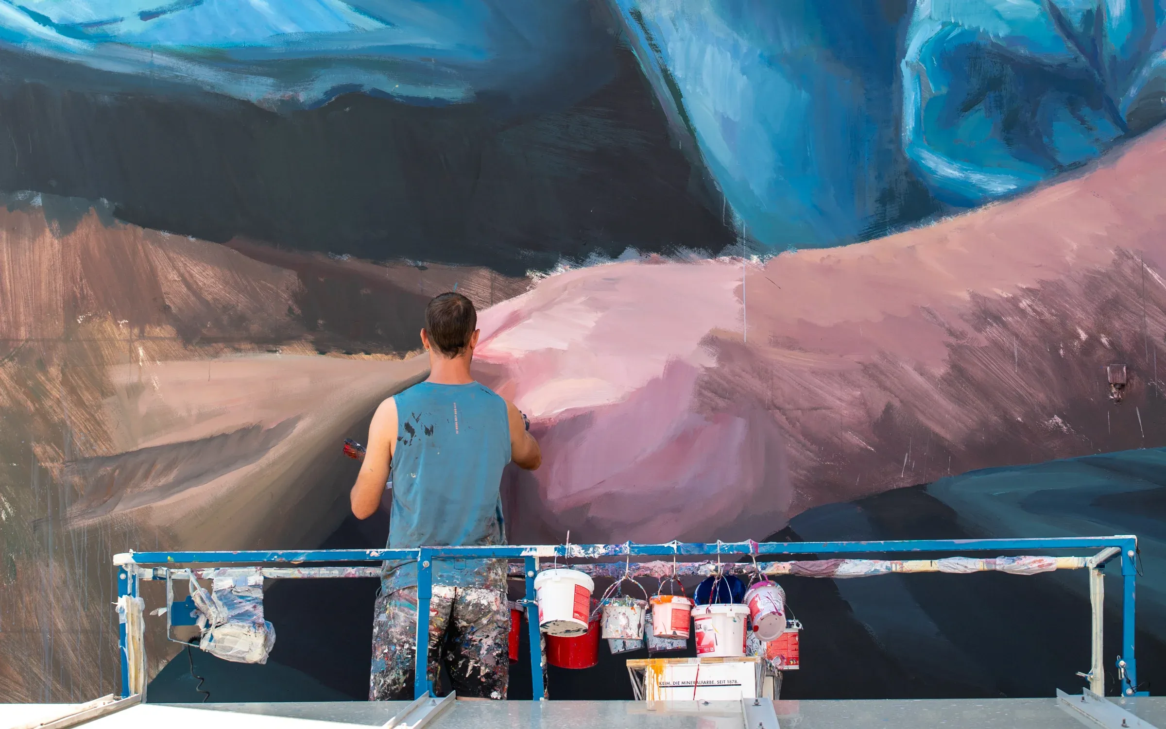 Slim Safont auf dem Gerüst vor dem halb fertigen Mural, Farbeimer am Geländer